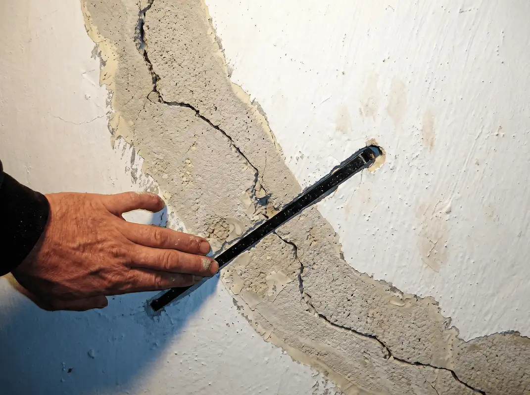 A wall with a large crack is being inspected by a professional in Fort Wayne, IN