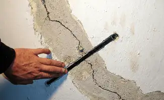A wall with a large crack is being inspected by a professional in Fort Wayne, IN